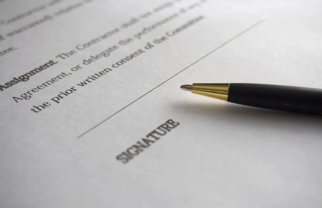 A black and gold pen resting beside an empty signature line on a printed agreement