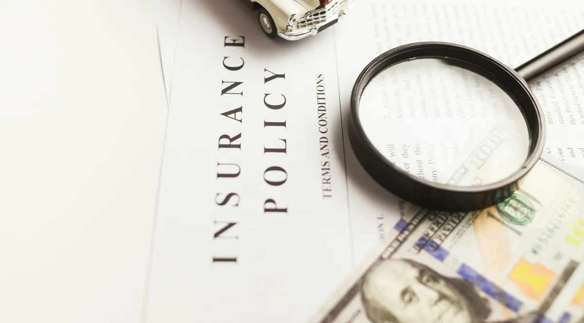 A toy classic car on an insurance policy, beside a magnifying glass and a 100 dollar bill