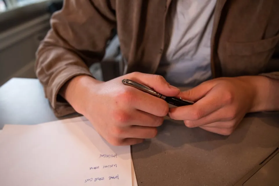 Hands holding a pen above a sheet of handwritten paper on a desk