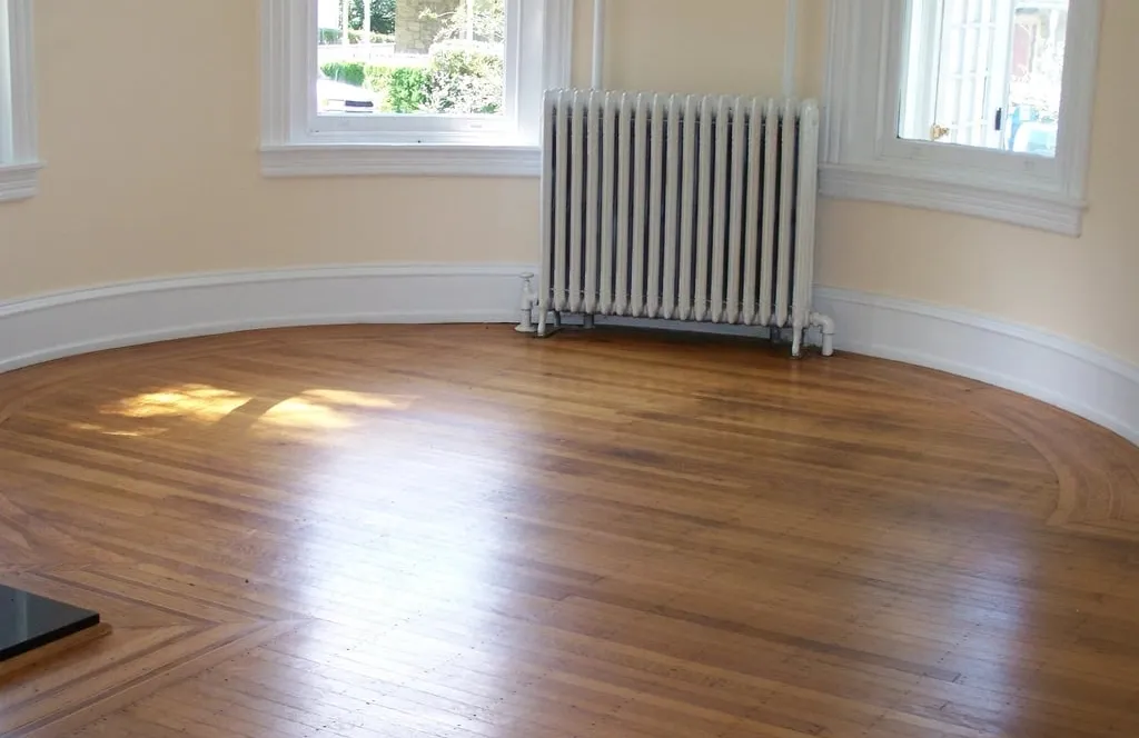 An empty room with a polished wooden floor, a white radiator and two tall windows