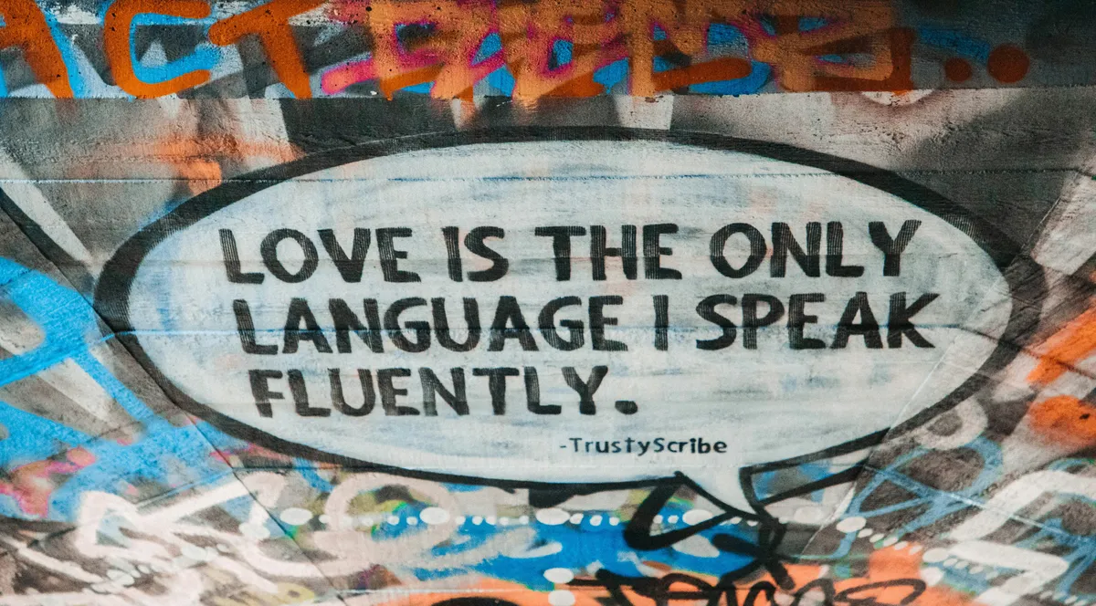 A graffiti speech bubble on a wall reading Love is the only language I speak fluently