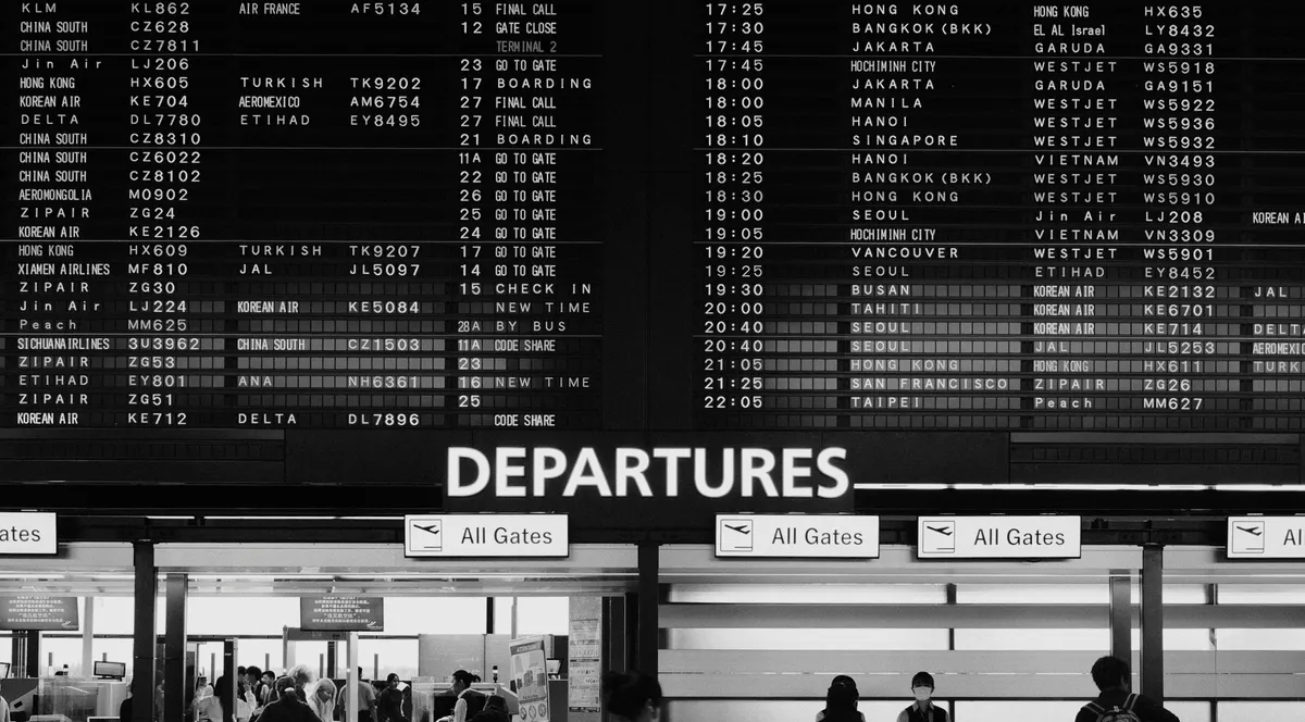 People walking past a departure board in an airport
