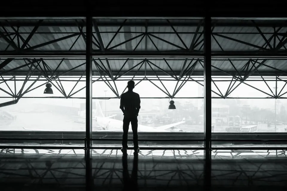 Silhouette of a traveler at an airport terminal window with a parked plane in the mist outside