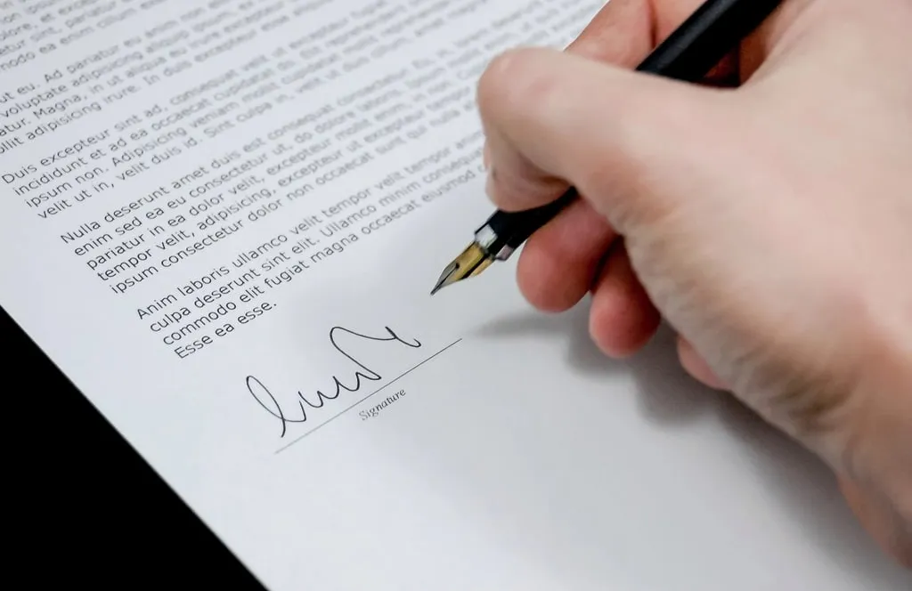 A hand signing a printed document with a fountain pen on the signature line