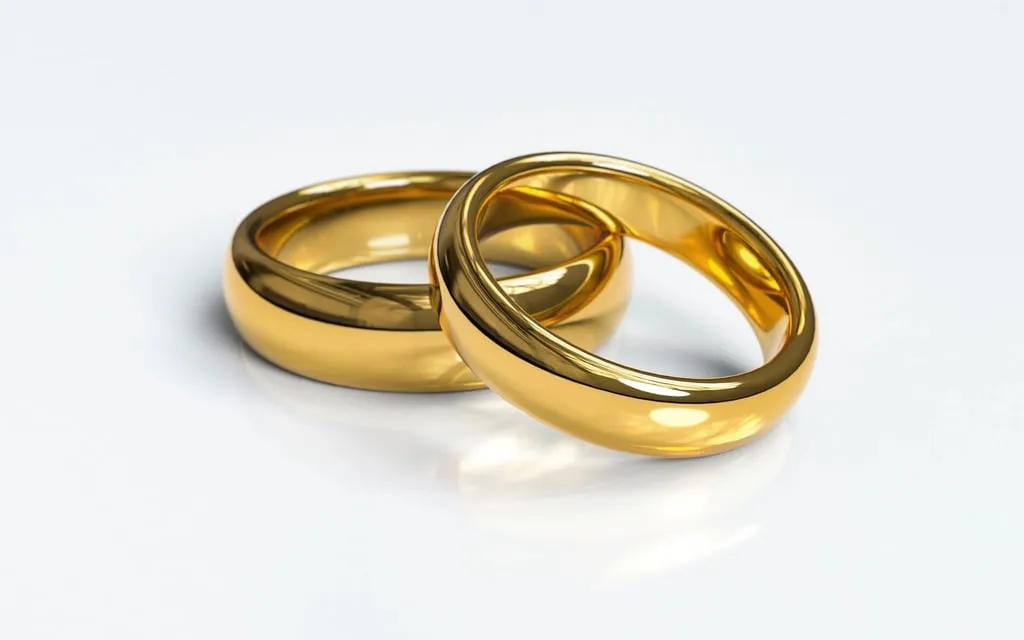 Two gold wedding rings resting against each other on a white surface