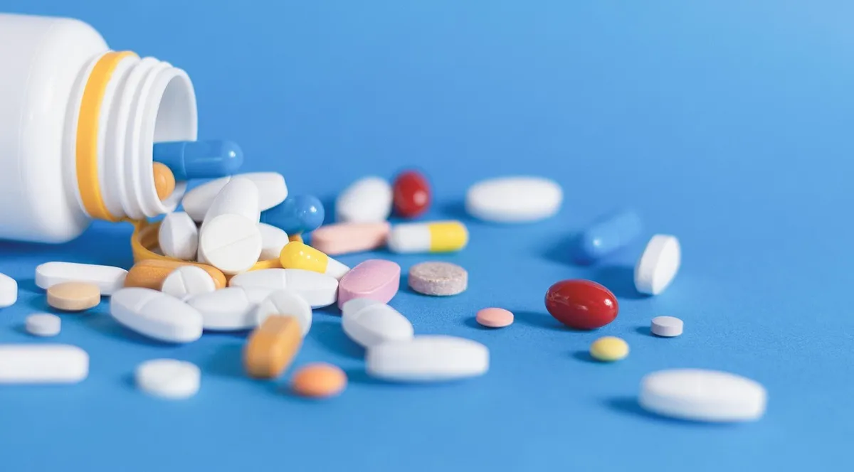 Colored pills and tablets spilling from a white bottle onto a blue surface