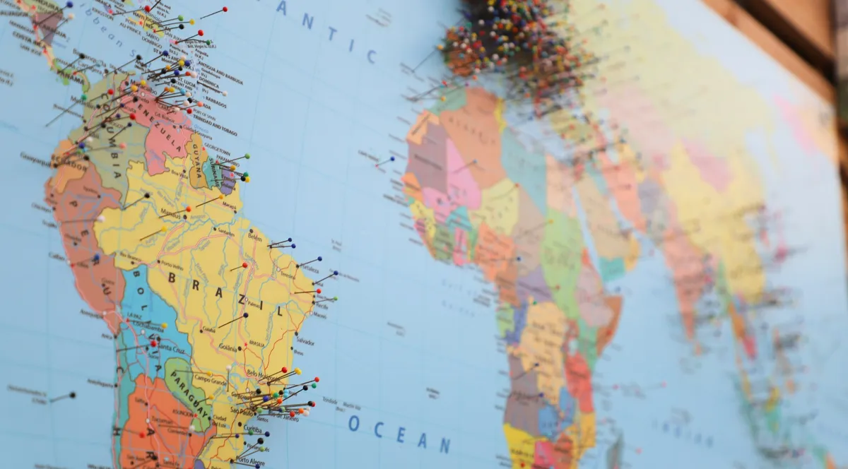 A world map on a wall with colored pins clustered over Europe