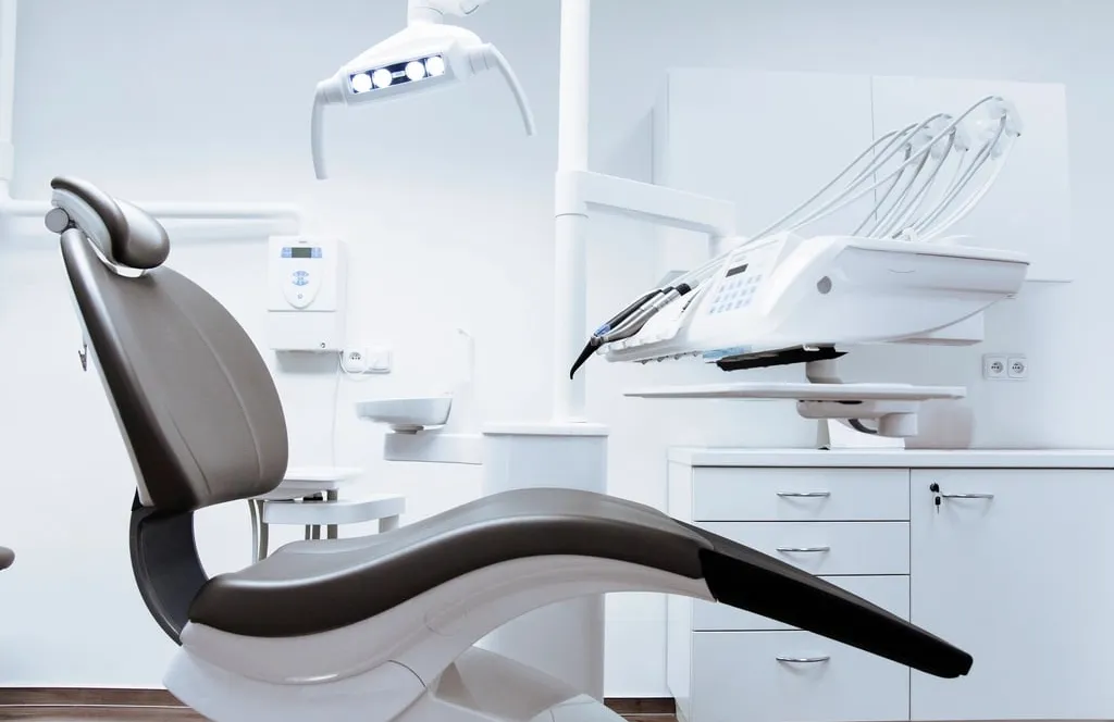 An empty dental chair and equipment in a bright white treatment room