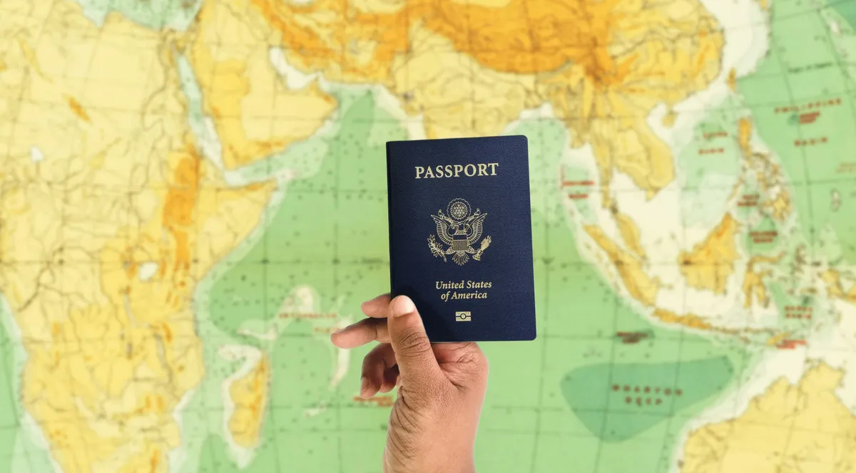 A hand holding up a U.S. passport in front of a world map