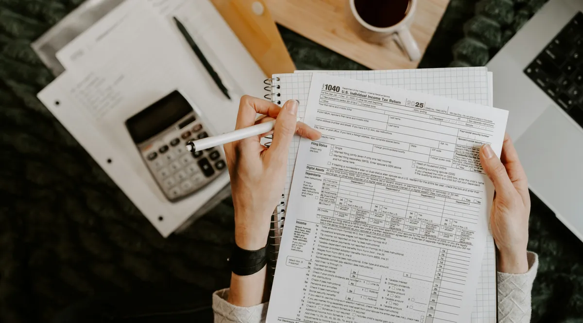 A person reviewing documents with a calculator and a laptop