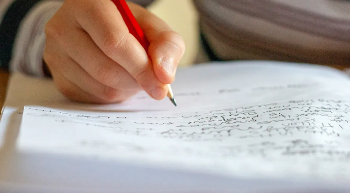 A hand writing in a notebook with a red pencil