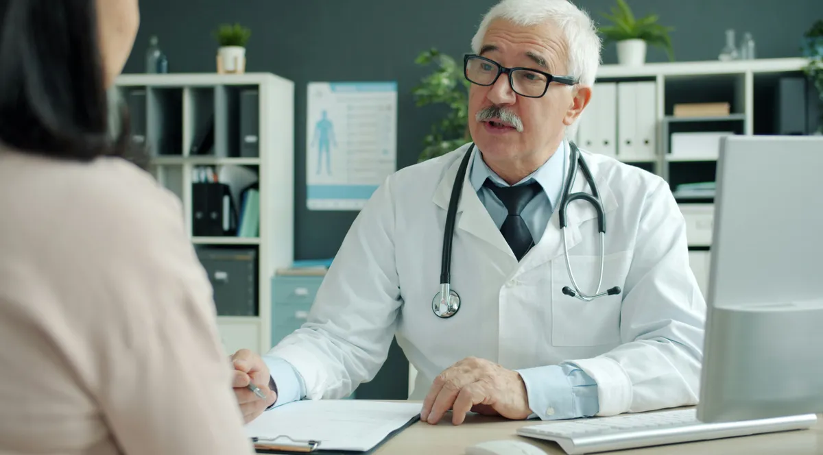 A doctor in a white coat talking with a patient across a desk
