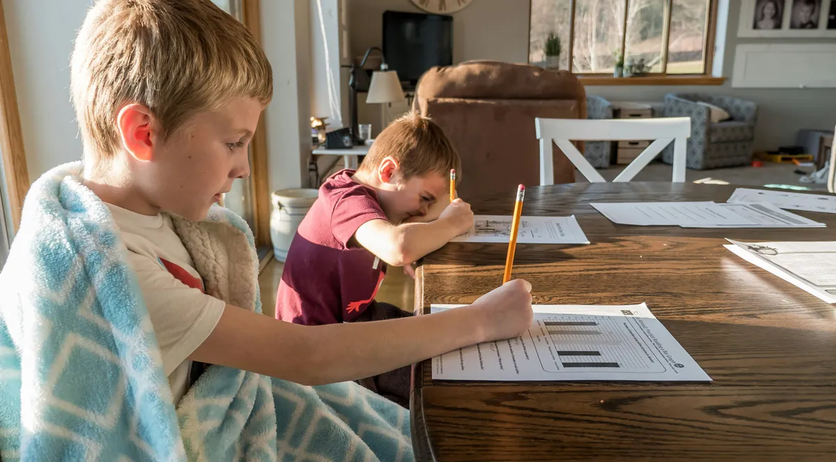 Two children doing schoolwork with pencils at a wooden table