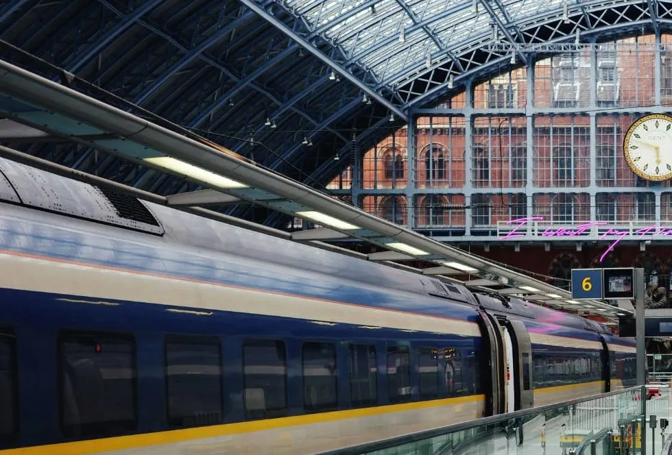 A blue and yellow high-speed train at a platform under the glass and iron roof of a station