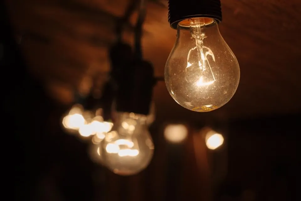 A clear light bulb glowing under a wooden ceiling, with more bulbs out of focus behind