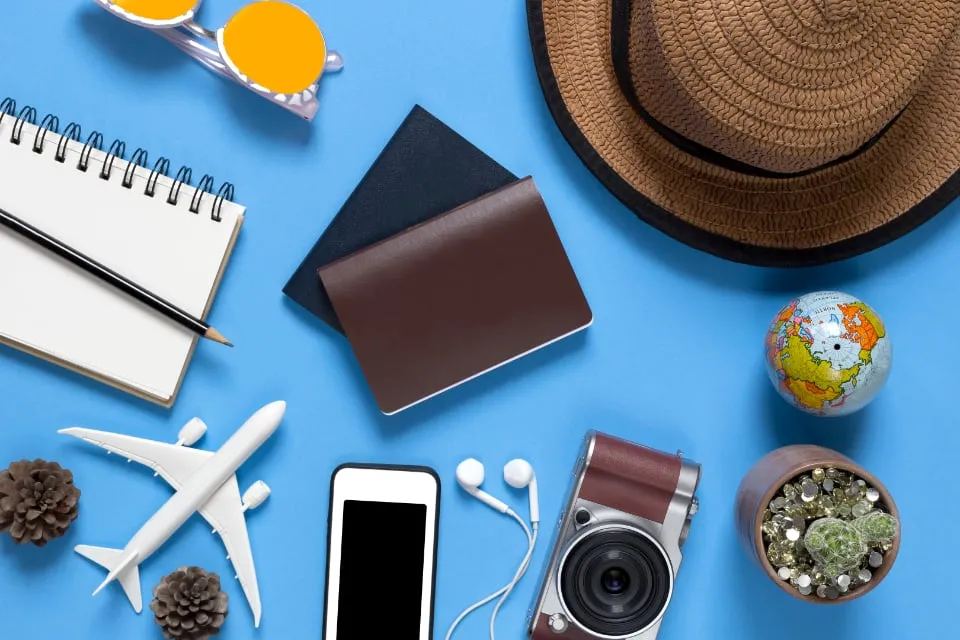 A brown passport, a notebook, a model airplane and sunglasses laid out on a blue table