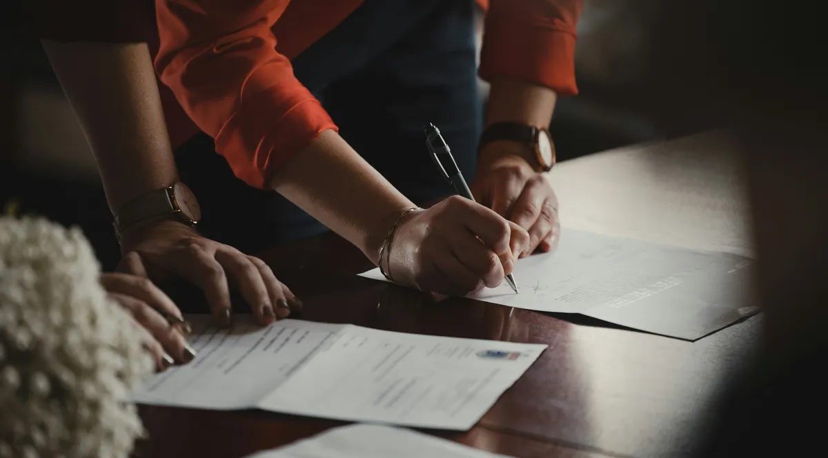 Two people signing documents at a wooden table