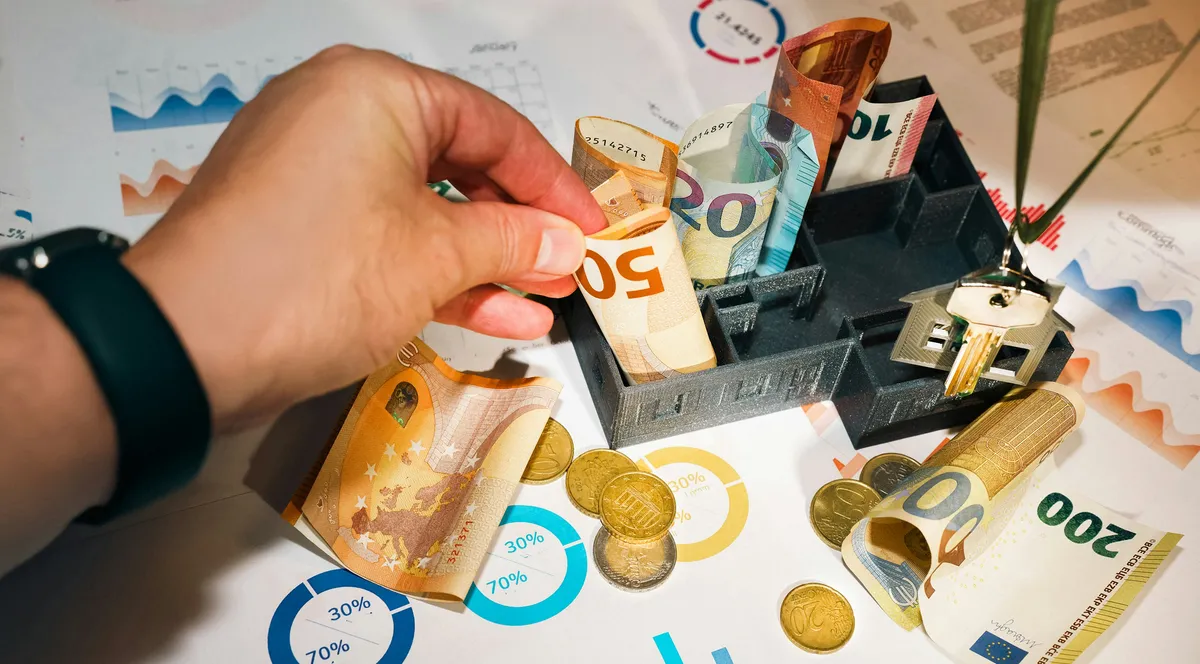 A hand putting money into a small model house