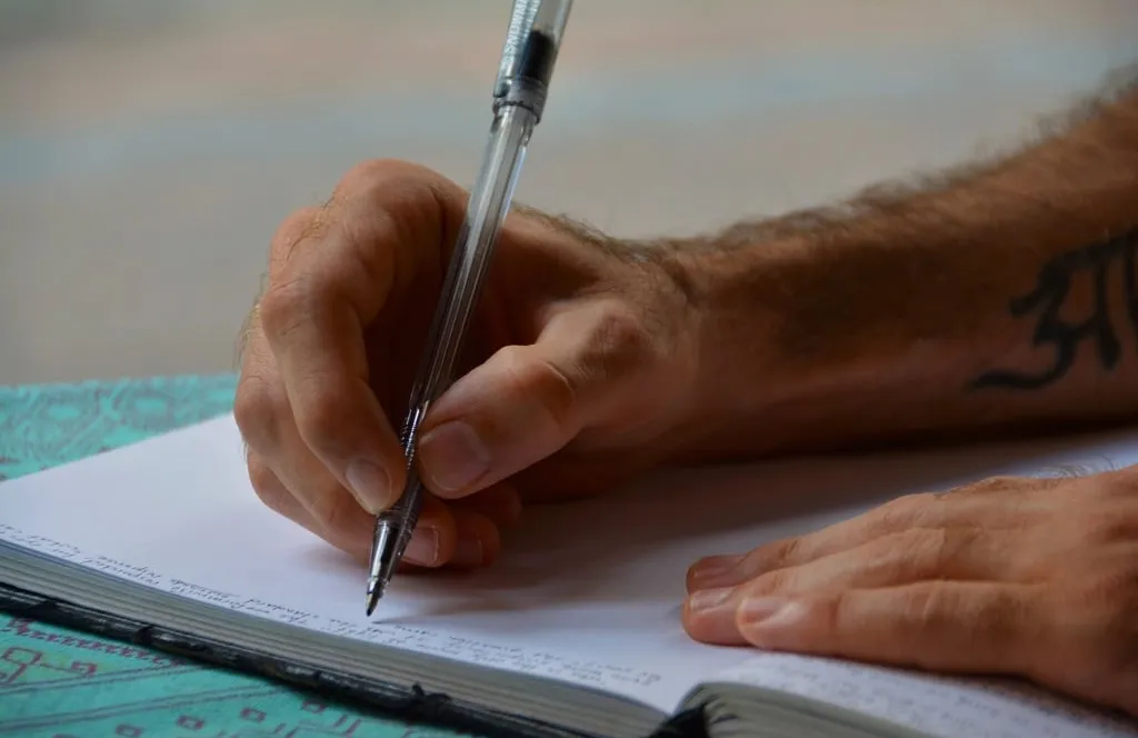 A hand writing with a pen in an open notebook on a table
